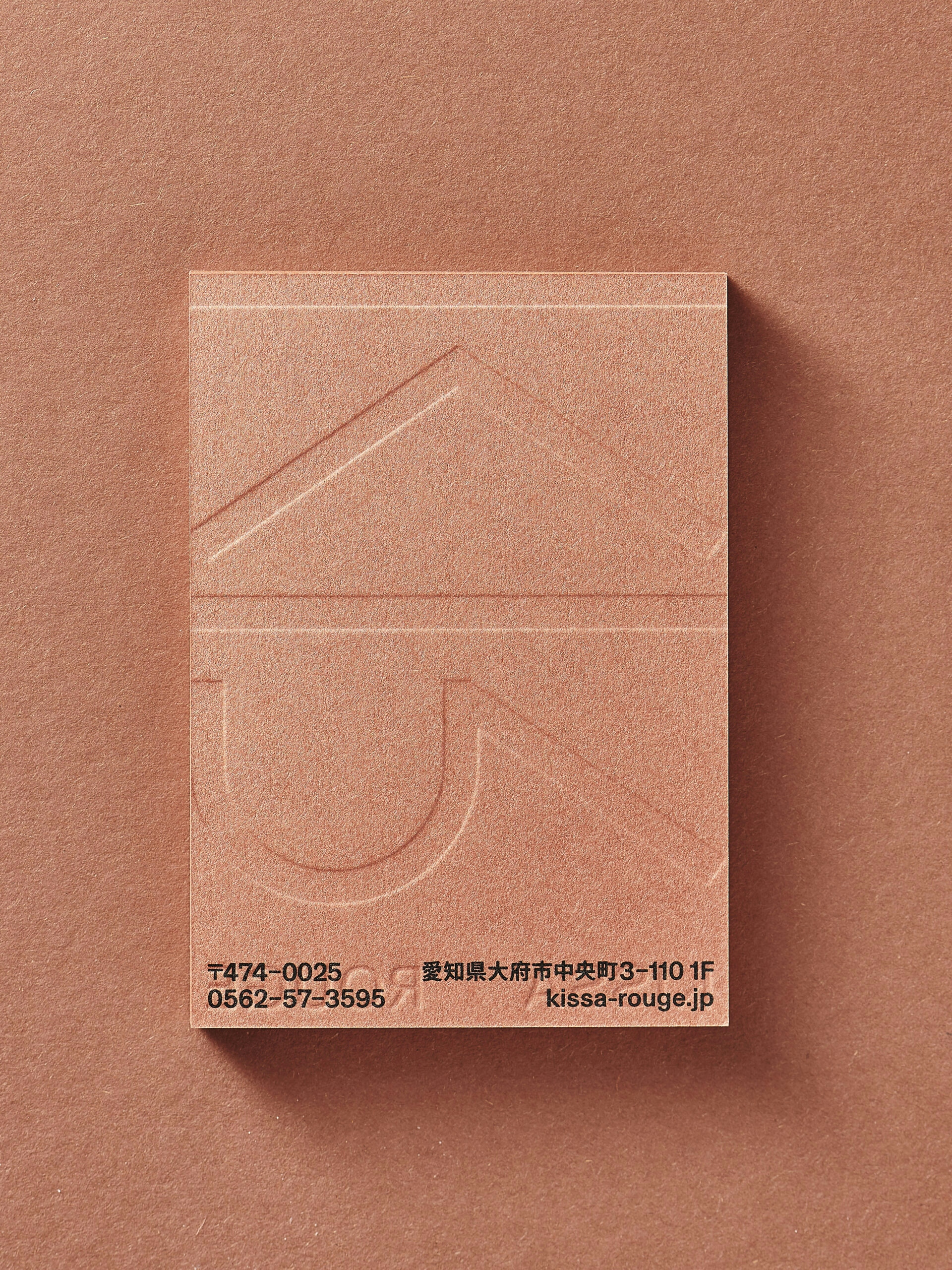 Kissa Rouge shop card front in earthy redish paper with a blind embossing back