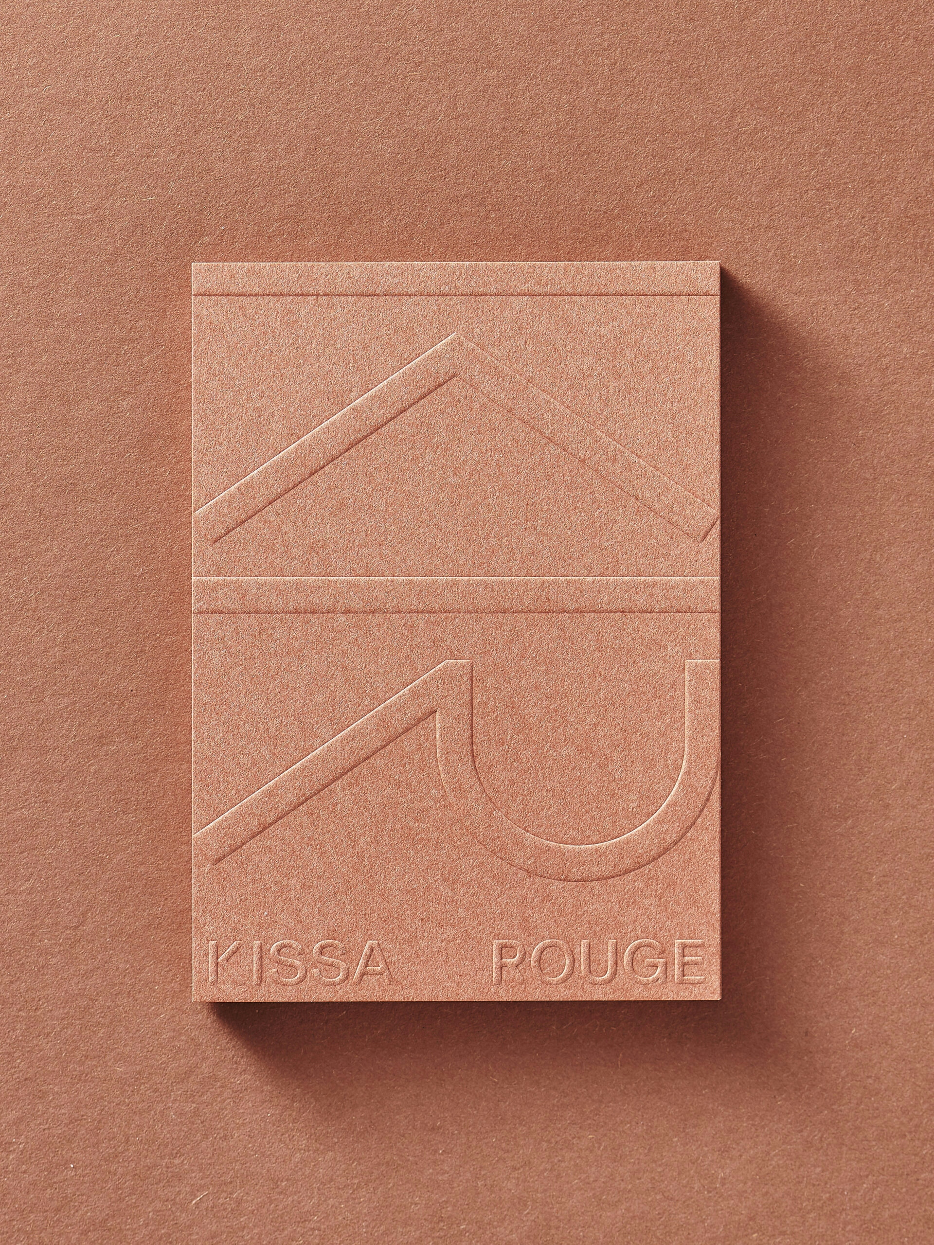 Kissa Rouge shop card front in earthy redish paper with a blind embossing